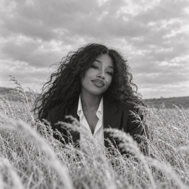 Unofficial AI-generated image of SZA: smiling among pale grass beneath a wide overcast sky.
